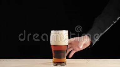 新鲜啤酒。 手从黑色背景的木桌上拿出一杯啤酒杯中的美味工艺啤酒。 冷鲜啤酒
